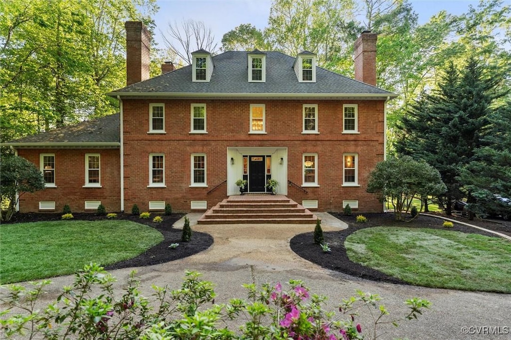 rear view of property with a lawn, brick siding, a chimney, and a shingled roof