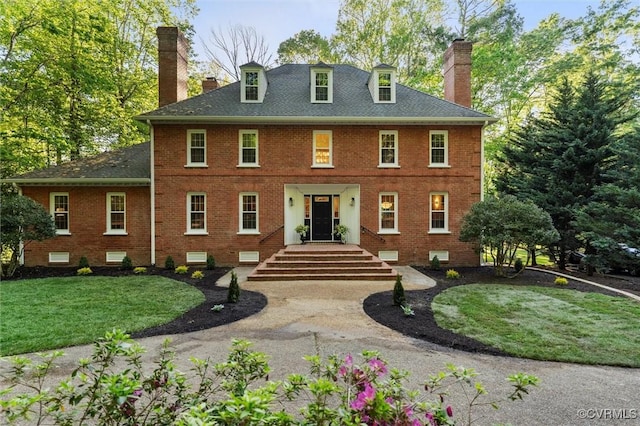 rear view of property with a lawn, brick siding, a chimney, and a shingled roof