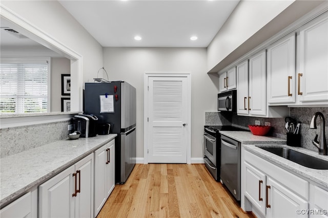 kitchen featuring black microwave, a sink, freestanding refrigerator, light wood finished floors, and dishwashing machine