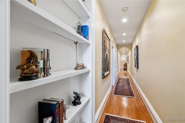 corridor featuring baseboards, recessed lighting, arched walkways, and wood finished floors