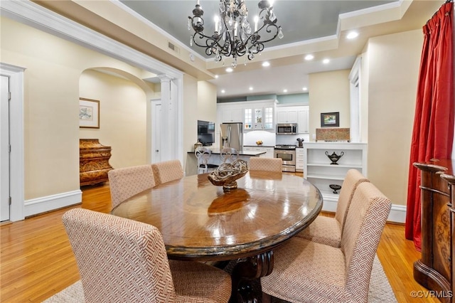 dining space featuring light wood-type flooring, ornamental molding, arched walkways, and a notable chandelier