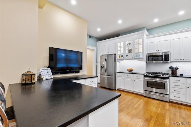 kitchen featuring backsplash, dark countertops, appliances with stainless steel finishes, a peninsula, and white cabinetry