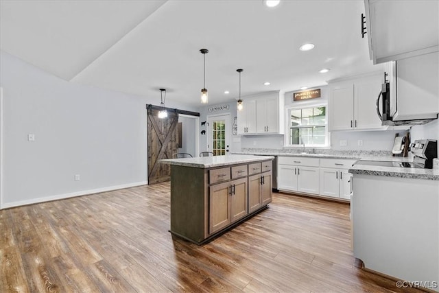 kitchen featuring light wood-style floors, appliances with stainless steel finishes, white cabinets, and a barn door