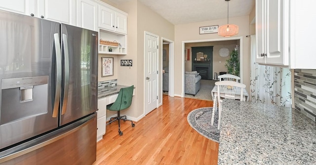 kitchen featuring light wood-style floors, tasteful backsplash, built in desk, white cabinets, and stainless steel fridge