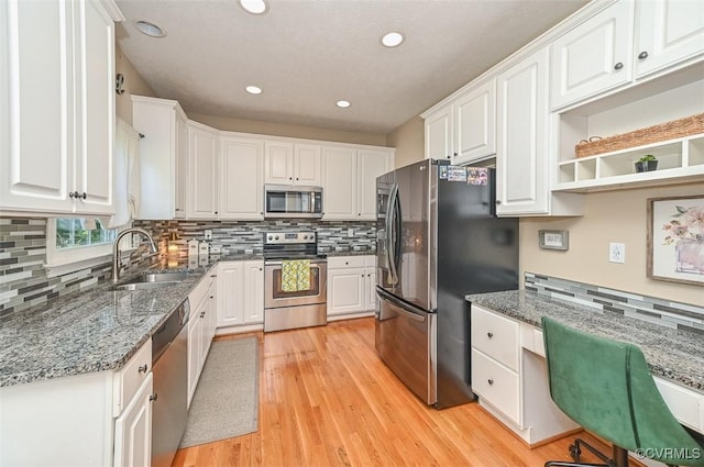 kitchen with decorative backsplash, white cabinetry, a sink, light wood finished floors, and appliances with stainless steel finishes