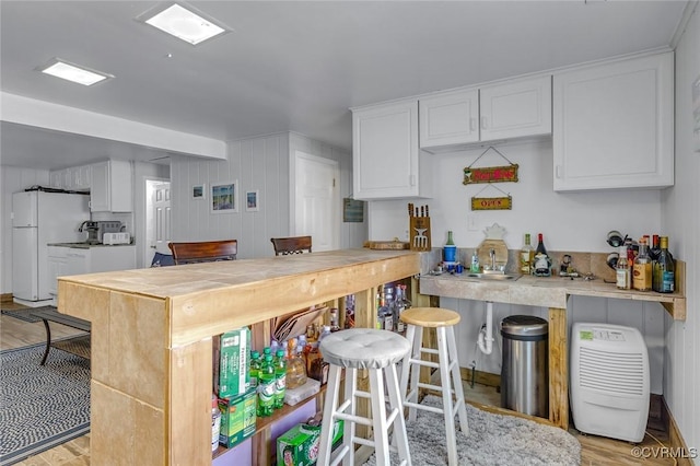 kitchen featuring white cabinets, light countertops, freestanding refrigerator, a kitchen bar, and light wood-style flooring