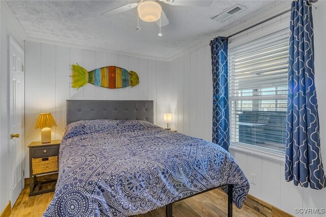 bedroom featuring a ceiling fan, a textured ceiling, light wood-style floors, baseboards, and visible vents