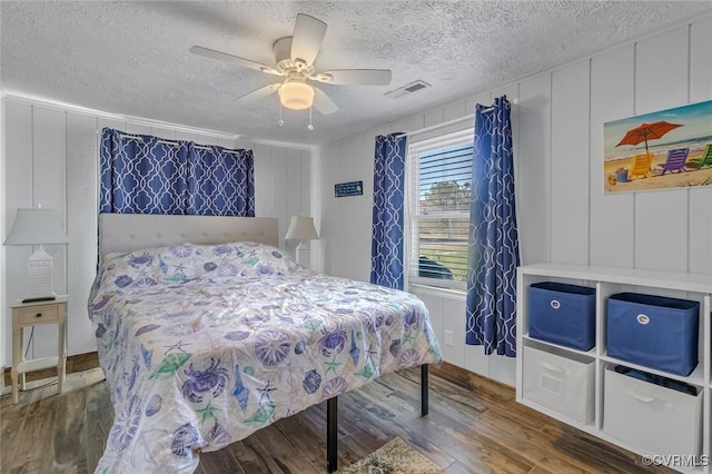 bedroom with a decorative wall, wood finished floors, visible vents, and a textured ceiling
