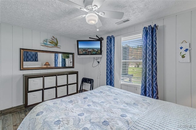 bedroom featuring wood finished floors, visible vents, a textured ceiling, and a decorative wall