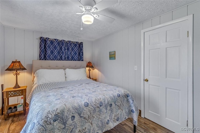 bedroom with wood finished floors, a textured ceiling, ceiling fan, and a decorative wall