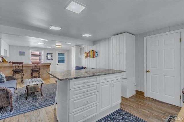 kitchen with light wood finished floors, a center island, white cabinetry, and light stone counters