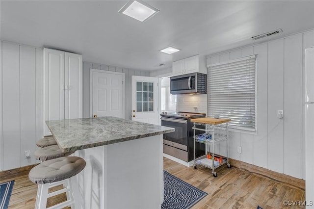 kitchen with white cabinets, a kitchen breakfast bar, visible vents, light wood-type flooring, and appliances with stainless steel finishes