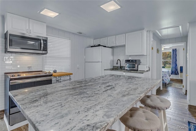 kitchen with light wood-type flooring, stainless steel appliances, light stone countertops, and backsplash