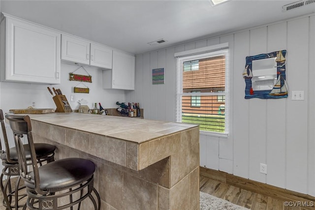 kitchen with white cabinets, a peninsula, visible vents, wood finished floors, and a breakfast bar area