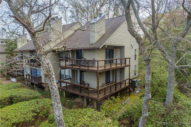 back of house featuring a shingled roof, a chimney, and a balcony