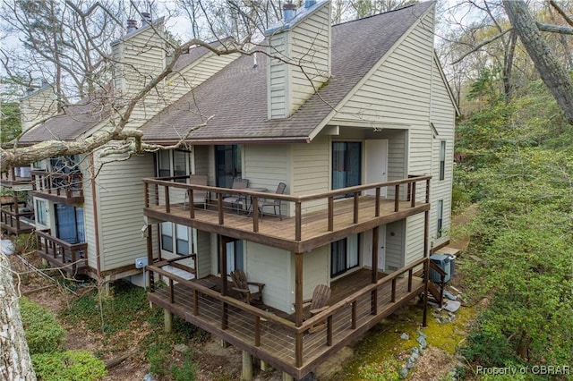 back of property featuring a chimney, central AC, a balcony, and a shingled roof