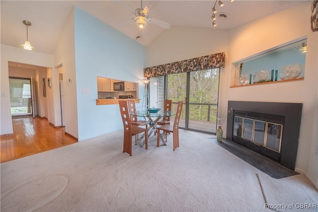 dining space featuring a fireplace with flush hearth, ceiling fan, high vaulted ceiling, and light colored carpet