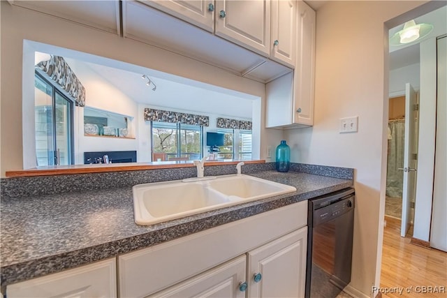kitchen featuring black dishwasher, dark countertops, light wood finished floors, and a sink