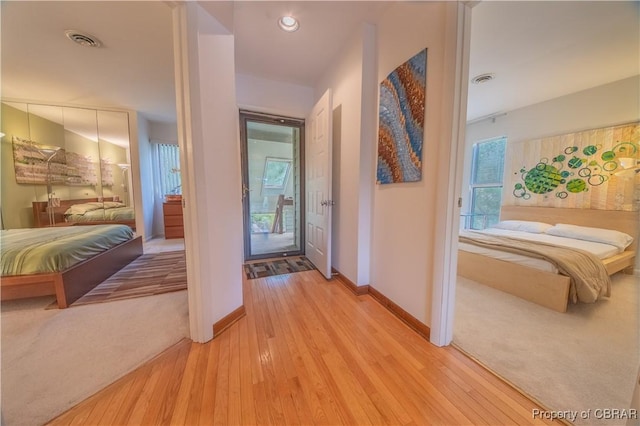 corridor with light colored carpet, baseboards, light wood-style floors, and visible vents