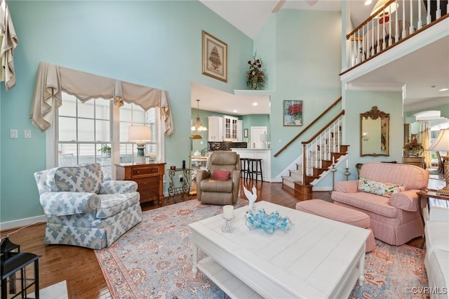 living room featuring a towering ceiling, baseboards, wood finished floors, and stairs