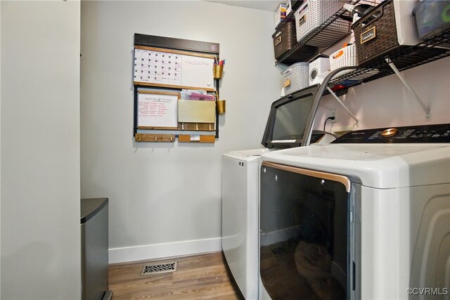 clothes washing area with laundry area, visible vents, wood finished floors, baseboards, and washer and clothes dryer