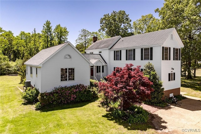 view of front facade featuring a shingled roof, a chimney, cooling unit, and a front yard