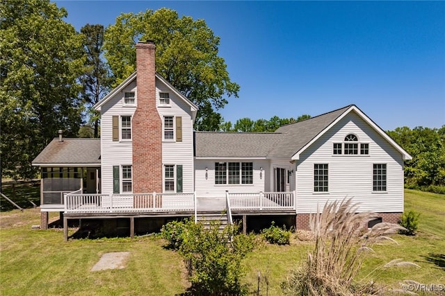 rear view of house with a wooden deck, a chimney, a sunroom, a shingled roof, and a yard