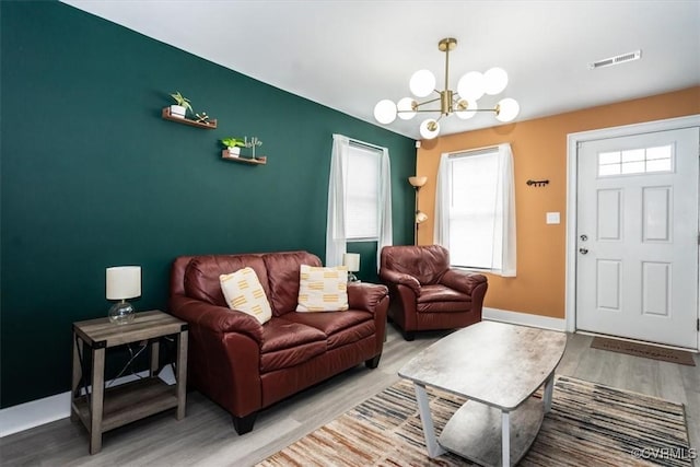 living area featuring a healthy amount of sunlight, an inviting chandelier, wood finished floors, and visible vents