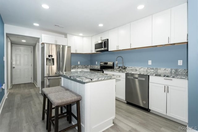 kitchen featuring appliances with stainless steel finishes, light stone counters, a sink, light wood finished floors, and a breakfast bar area