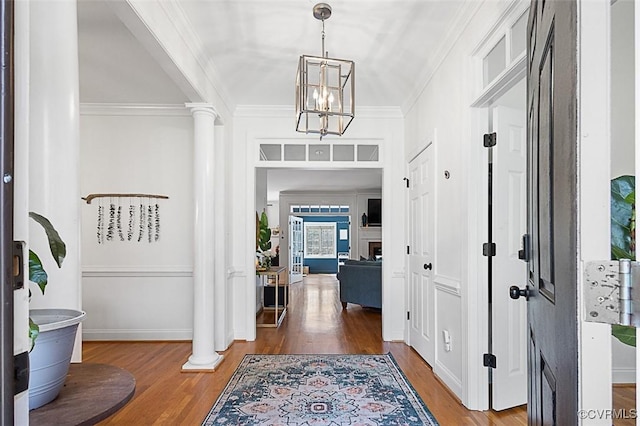 entrance foyer with an inviting chandelier, ornate columns, wood finished floors, and crown molding