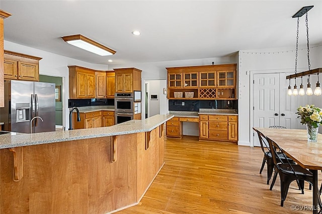 kitchen featuring a breakfast bar area, brown cabinets, appliances with stainless steel finishes, and light wood-type flooring