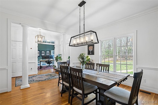 dining room with light wood-type flooring, crown molding, a chandelier, and ornate columns