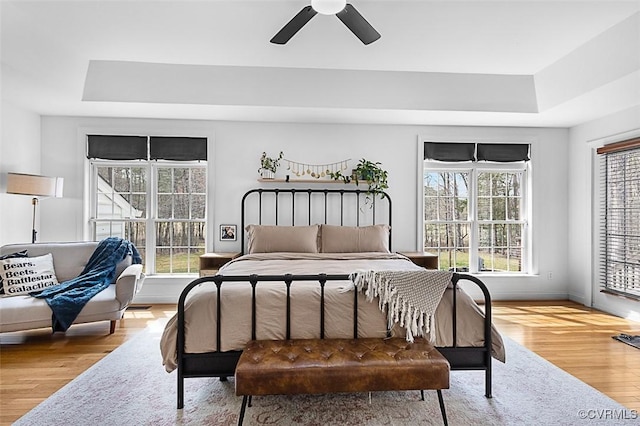 bedroom featuring wood finished floors, a ceiling fan, a tray ceiling, and baseboards
