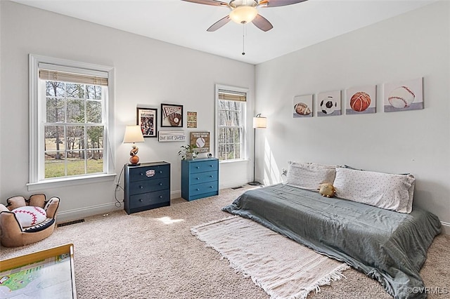 carpeted bedroom featuring visible vents, multiple windows, a ceiling fan, and baseboards