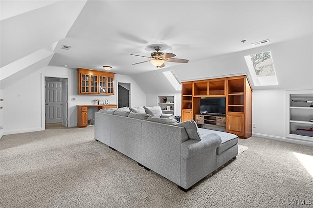 living room featuring light colored carpet, built in shelves, visible vents, a ceiling fan, and lofted ceiling with skylight