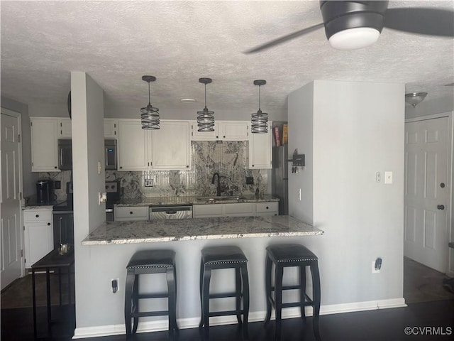 kitchen featuring a peninsula, stainless steel dishwasher, decorative backsplash, and a sink