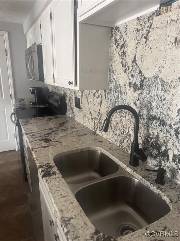 details with white cabinets, light stone countertops, a sink, and stainless steel microwave