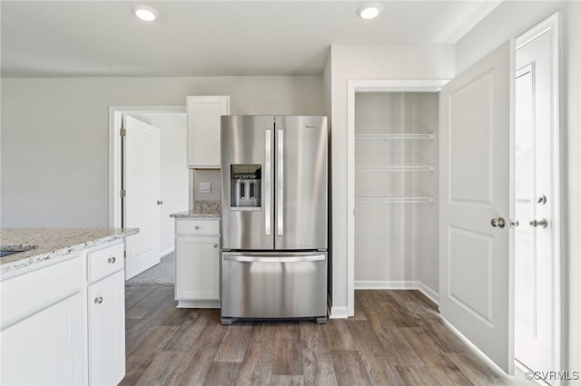 kitchen featuring white cabinets, stainless steel fridge, wood finished floors, and light stone counters
