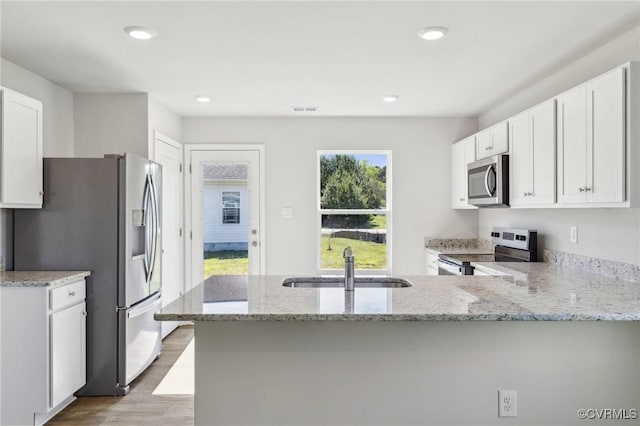 kitchen with light stone counters, wood finished floors, a sink, white cabinets, and appliances with stainless steel finishes