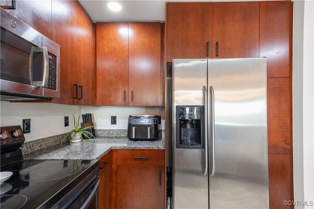 kitchen featuring dark stone counters, brown cabinets, stainless steel appliances, and recessed lighting