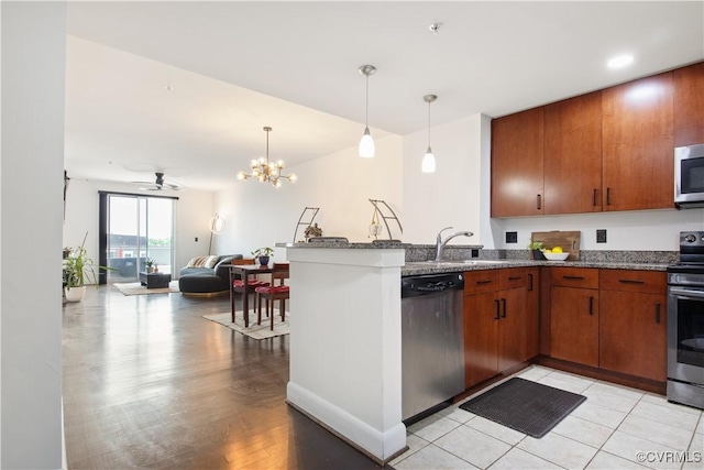 kitchen with stainless steel appliances, a peninsula, a sink, dark stone counters, and open floor plan