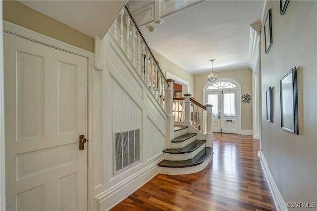 foyer featuring an inviting chandelier, dark wood finished floors, visible vents, ornamental molding, and stairway