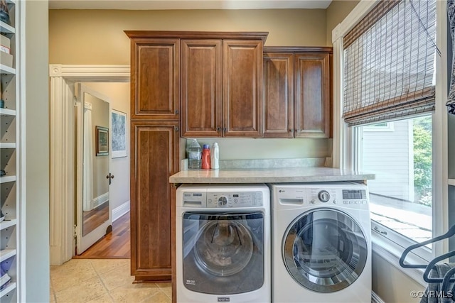clothes washing area featuring light tile patterned floors, washing machine and dryer, and cabinet space