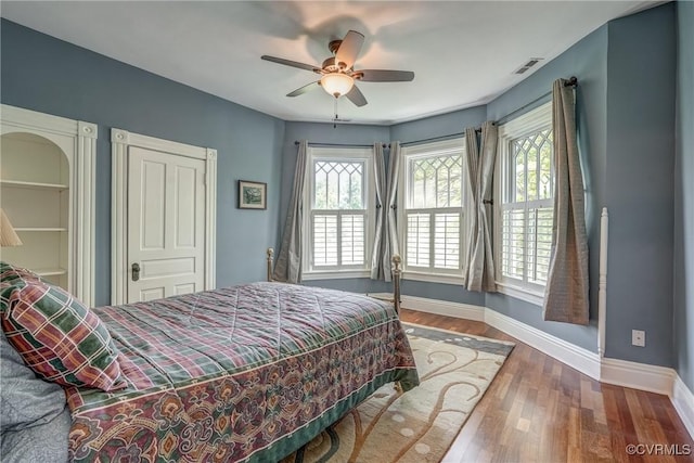 bedroom with baseboards, wood finished floors, visible vents, and multiple windows