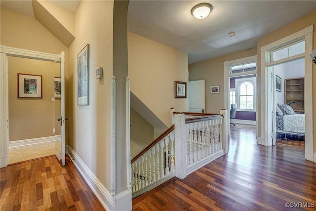 corridor featuring baseboards, an upstairs landing, and wood finished floors
