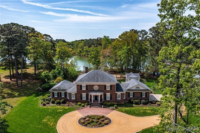 colonial inspired home featuring brick siding, a water view, a front lawn, and curved driveway
