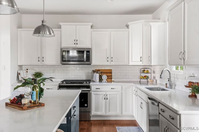 kitchen featuring dark wood-style flooring, pendant lighting, a sink, white cabinets, and stainless steel appliances