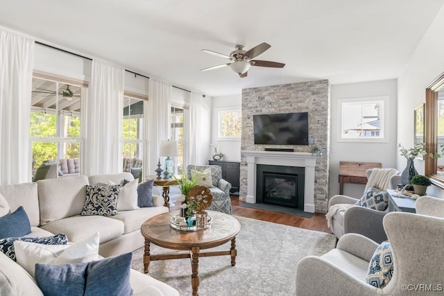 living area with a ceiling fan, a stone fireplace, and wood finished floors