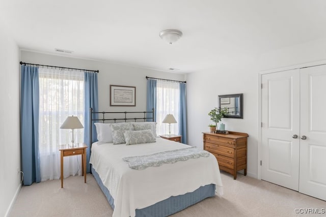 bedroom featuring light colored carpet, baseboards, visible vents, and a closet