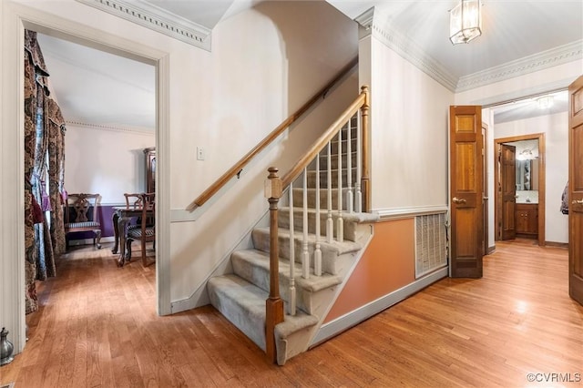 stairway featuring wood finished floors, crown molding, and baseboards